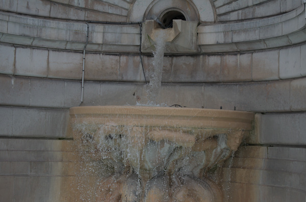 A gothic fountain with a spout above a sculpted bowl. Water is flowing from the spout and falling into the overflowing bowl.