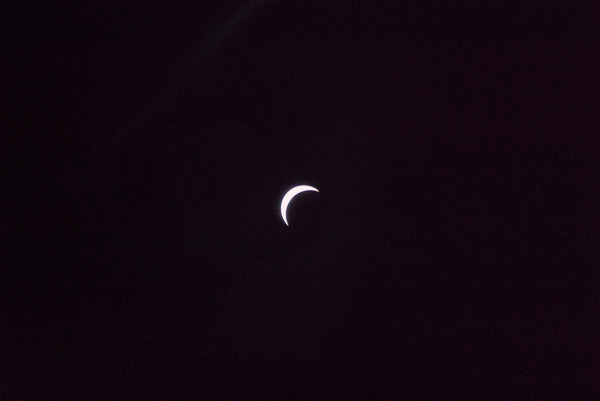 A photograph of the partial
							eclipse. The sun appears as a bright white crescent, with the moon
							invisible. The photo appears to resemble a crescent moon.